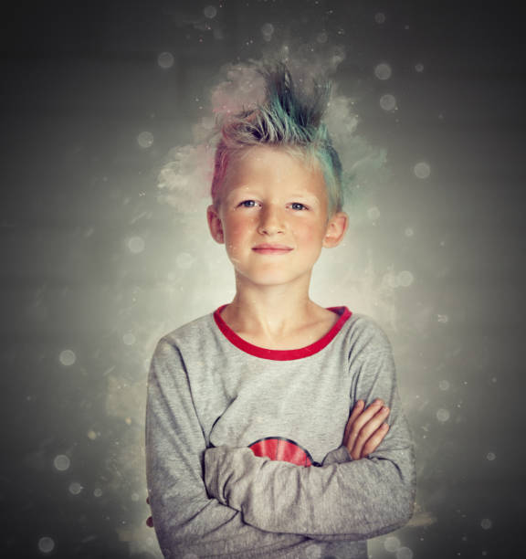 A 6 year old blond boy missing his two front teeth looks up and smiles in front of black background