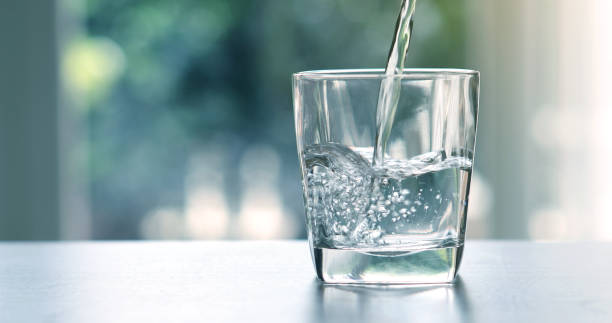 chiudere l'acqua di bevanda fresca purificata versando dalla bottiglia sul tavolo in soggiorno - acqua foto e immagini stock