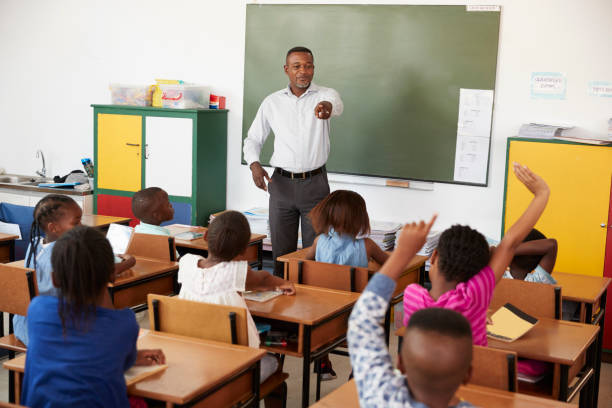 istock Teacher and kids with hands up in an elementary school class 803155640