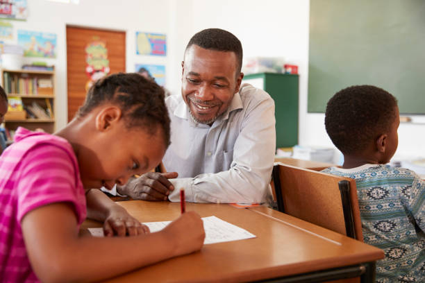 istock Black male teacher helping elementary school girl in class 803170686