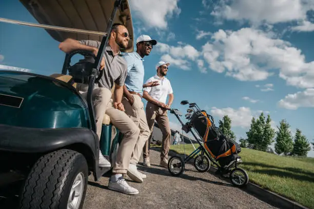 group of smiling friends standing near golf cart and looking away