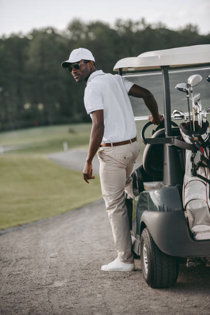 chic homme afro-américain debout près de voiturette de golf sur le parcours de golf - golf cart golf mode of transport transportation photos et images de collection