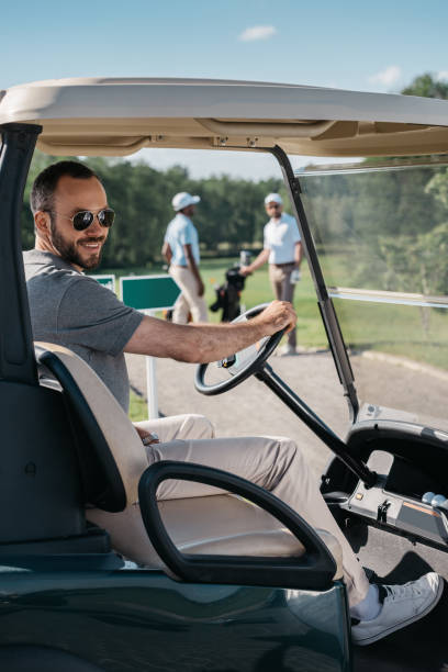 jovem homem caucasiano em copos sorrindo enquanto está sentado no carrinho de golfe - golf course golf people sitting - fotografias e filmes do acervo