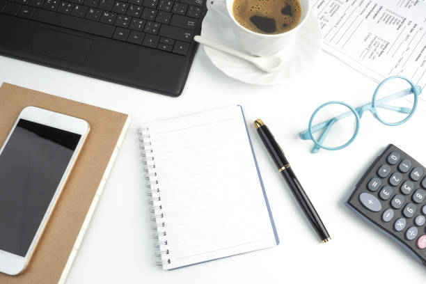 istock Blank page notebook on white desktop with pen, coffee, laptop, book, calculator, glasses and mobile phone, top view, business desktop, modern and relax feeling 803193080