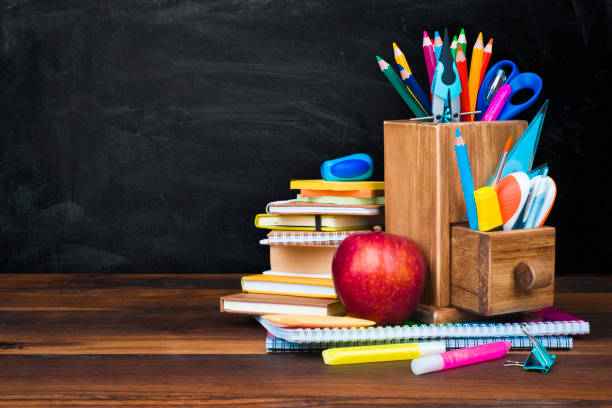 школьные принадлежности и аксессуары на деревянном столе на фоне доски - book brown apple education стоковые фото и изображения