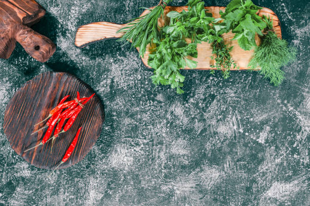 Fresh herbs for cooking Fresh chili peppers on the cutting board. Fresh cilantro, dill, oregano, thyme, tarragon and lemon balm potherbs ready for cooking. Dark grey spotty background. Top view tarragon cutting board vegetable herb stock pictures, royalty-free photos & images