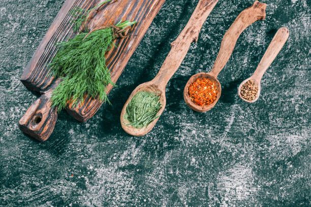 Fresh and dried herbs Fresh dill on wooden cutting board and dried spices in wooden spoons over dark gray spotty background. Top view tarragon cutting board vegetable herb stock pictures, royalty-free photos & images