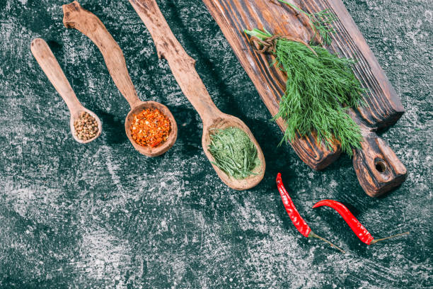 Fresh and dried herbs Fresh dill on wooden cutting board and dried spices in wooden spoons over dark gray spotty background. Top view tarragon cutting board vegetable herb stock pictures, royalty-free photos & images