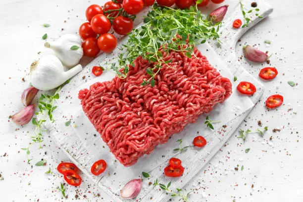 Fresh Raw Beef Minced Meat with salt, pepper, chilli and fresh thyme on white board