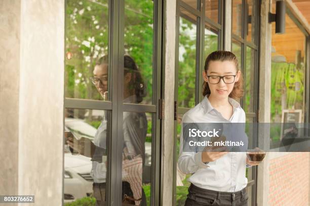 Half Thai Half American Business Woman Hold Iphone In Right Hand And Glass Of Hot Black Coffee In Left Hand Standing Against Glass Door At Coffee Shop Stock Photo - Download Image Now