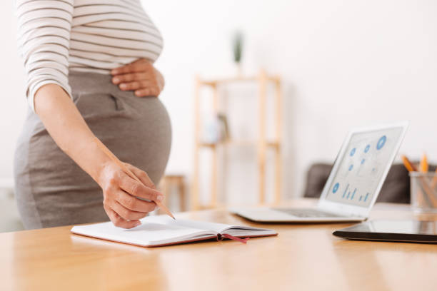 istock Pleasant pregnant woman making notes in the office 803284750