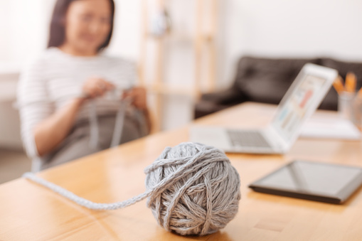 My hobby. Close up of ball of yarn lying on the table while pleasant pregnant woman knitting in the office
