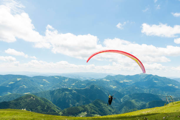 One Paraglider with red parachut flying over green hils against blue sky.