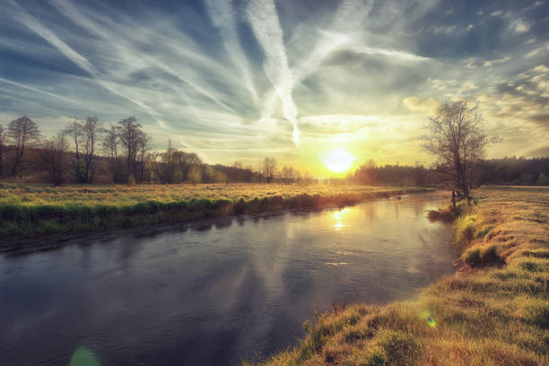 A beautiful sunrise over river in golden autumn morning. Naked trees on river bank and forest in distance on horizon