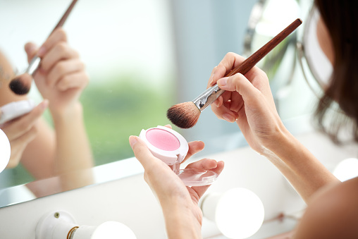 Young blonde woman putting on makeup, she is smiling, looking happy