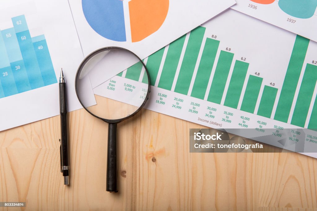 Lupe und Dokumente mit Analytics-Daten liegen auf Holztisch - Lizenzfrei Analysieren Stock-Foto