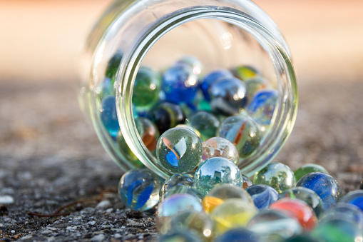 Glass jar full of marbles, fallen on the street. View of jar at an angle.


