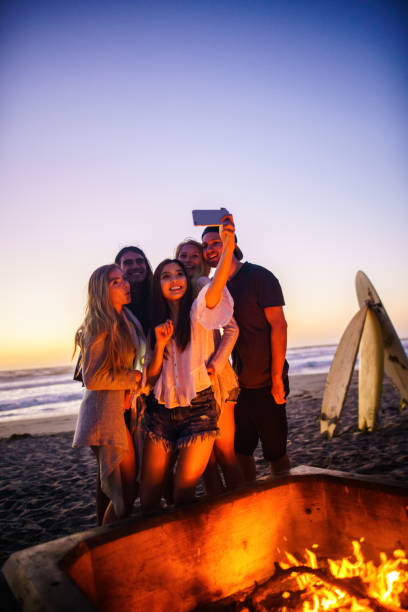 istock Multi ethnic group of young people, spending time watching sunset at the beach in San Diego, playing guitar and warming themselves by the fire 803375140