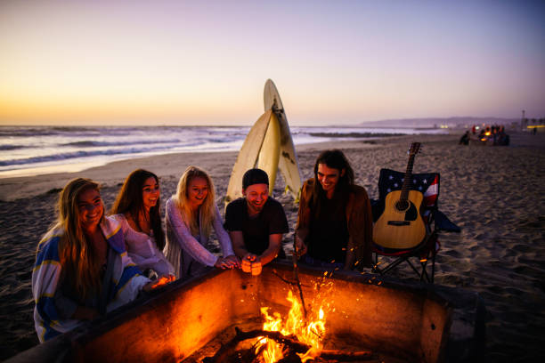 istock Multi ethnic group of young people, spending time watching sunset at the beach in San Diego, playing guitar and warming themselves by the fire 803384172
