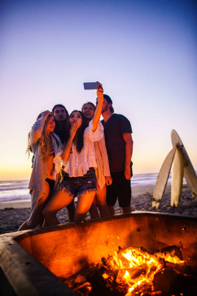 istock Multi ethnic group of young people, spending time watching sunset at the beach in San Diego, playing guitar and warming themselves by the fire 803386884