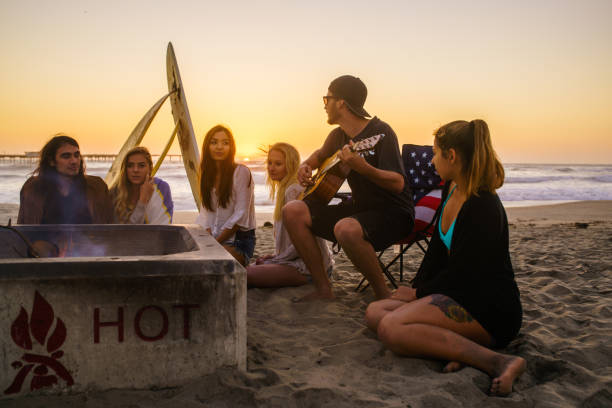 istock Multi ethnic group of young people, spending time watching sunset at the beach in San Diego, playing guitar and warming themselves by the fire 803387200