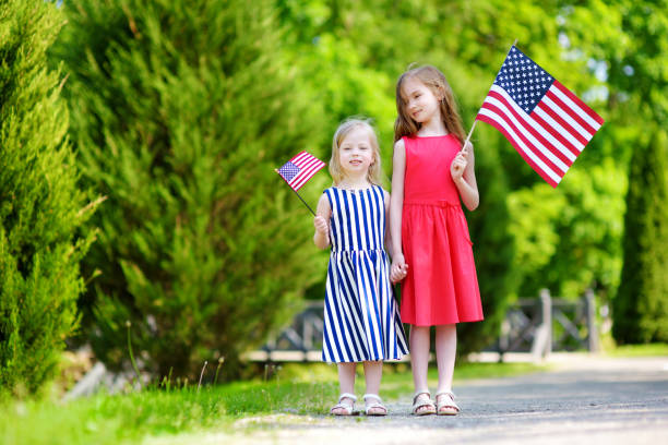 two adorable little sisters holding american flags outdoors on beautiful summer day - child flag fourth of july little girls imagens e fotografias de stock