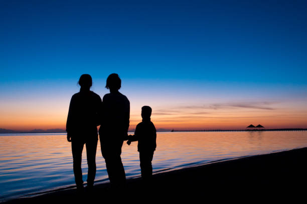 istock silhouette of three people standing on the beach in sunrise 803409600