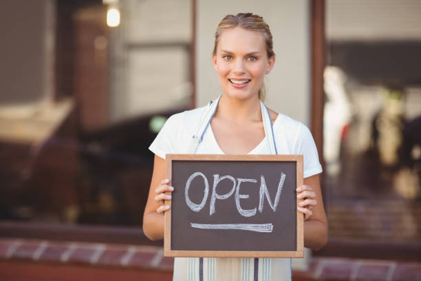 istock Smiling waitress showing chalkboard with open sign 803420136