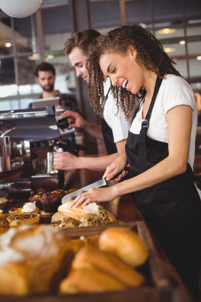 istock Smiling waitress cutting bread in front of colleague 803476296