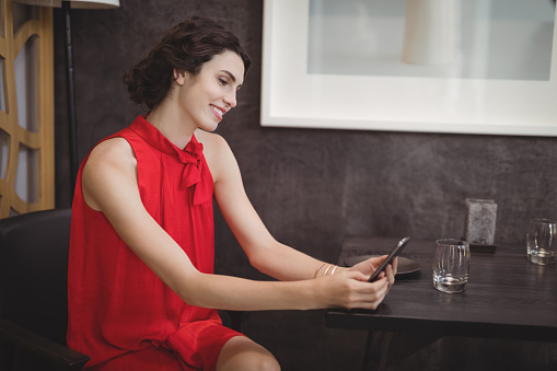 Beautiful woman using mobile phone at table in restaurant
