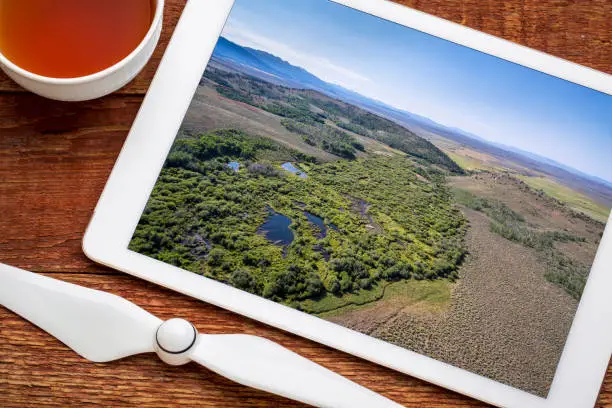reviewing aerial pictures of a stream at foothills of Medicine Bow Mountains (North Park, Colorado) on a digital tablet with a cup of tea