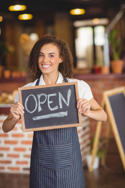 istock Smiling waitress showing chalkboard with open sign 803497610