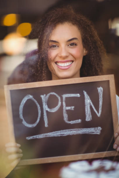 istock Smiling waitress showing chalkboard with open sign 803500226