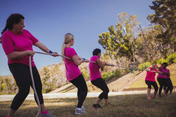 istock Group of women playing tug of war during obstacle course training 803500690