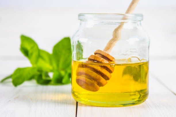 istock A honey jar with a spoon on a white table. In the background, mint. 803503370