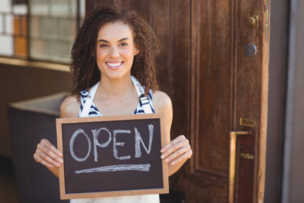 istock Smiling waitress showing chalkboard with open sign 803524468