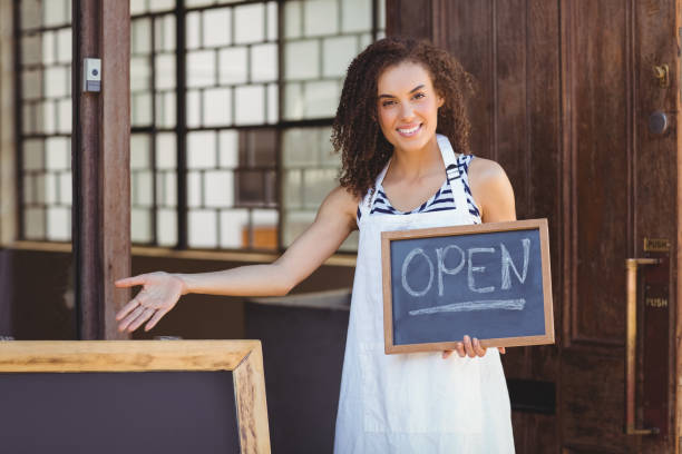 istock Smiling waitress showing chalkboard with open sign 803524492