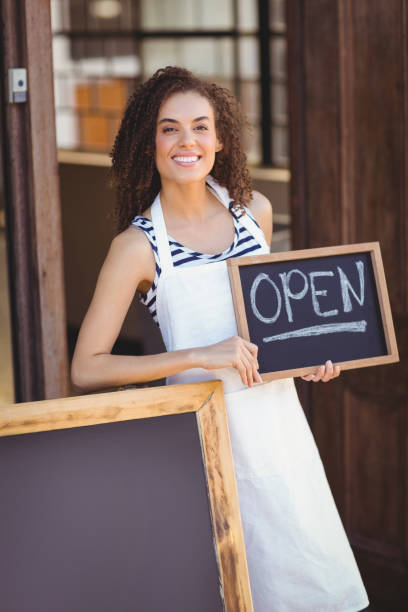 istock Smiling waitress showing chalkboard with open sign 803524500