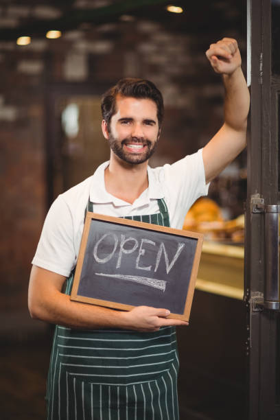 istock Smiling waiter showing chalkboard with open sign 803525264