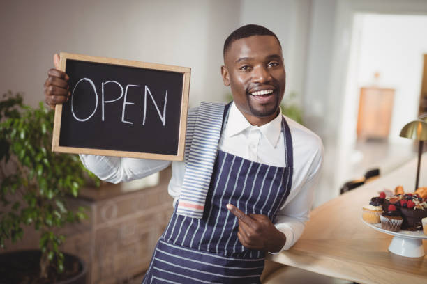 istock Smiling waiter showing chalkboard with open sign 803594188