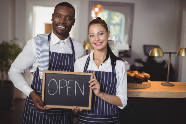 istock Smiling waiter and waitress showing chalkboard with open sign 803594344