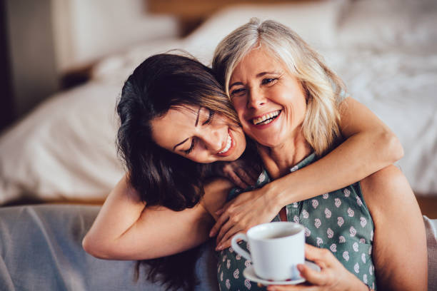 Loving adult daughter embracing cheerful senior mother at home Beautiful adult granddaughter hugging beautiful senior grandmother while sitting on the sofa dinking coffee coffee break photos stock pictures, royalty-free photos & images
