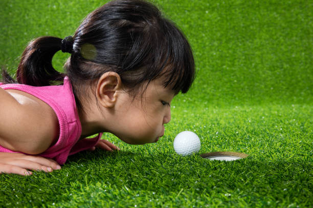 Asian Chinese little girl blowing the ball into a hole Asian Chinese little girl lying on grass and blowing the ball into a hole golf concentration stock pictures, royalty-free photos & images