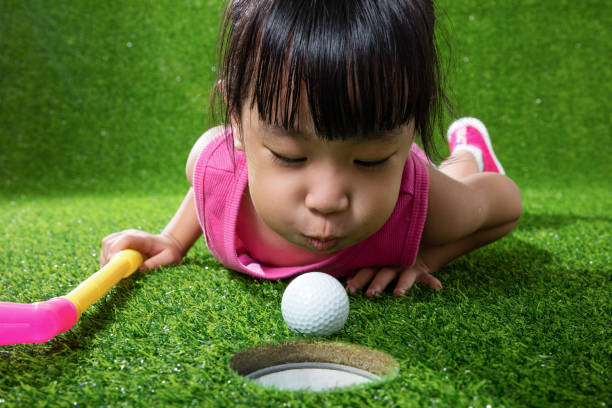 azjatycka chińska dziewczynka dmuchanie piłkę w dziurę - golf child sport humor zdjęcia i obrazy z banku zdjęć