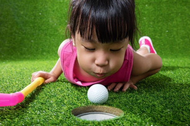 азиатская китайская маленькая девочка дует мяч в отверстие - golf child sport humor стоковые фото и изображения