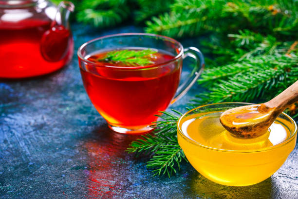Honey, tea and evergreen twigs Glass bowl of honey, herbal tea in teapot and evergreen fir tree twigs over spotty blue background. Close up pine needle tea stock pictures, royalty-free photos & images