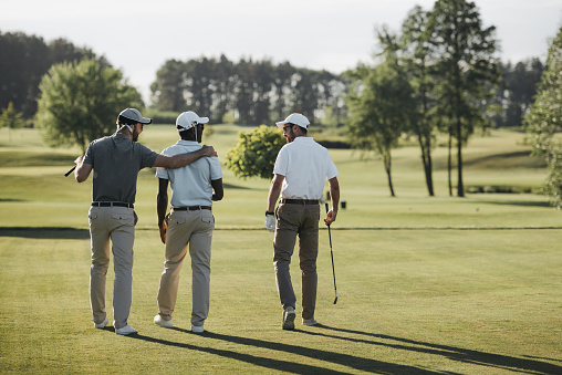 back view of multiethnic golf players hugging and walking on golf course