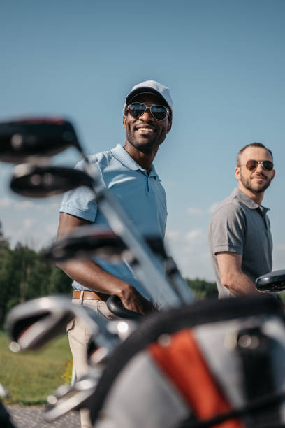 smiling multiethnic sportsmen going to the golf course, bag with clubs on foreground smiling multiethnic sportsmen going to the golf course, bag with clubs on foreground golf course photos stock pictures, royalty-free photos & images