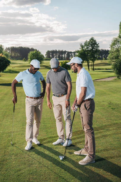istock Multiethnic group of golfers holding clubs and talking while standing on green grass 803639674