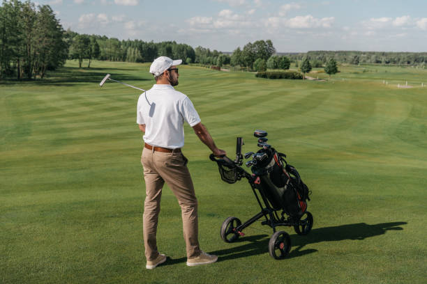 istock young golf player looking away while standing with bag and club on green pitch 803640484